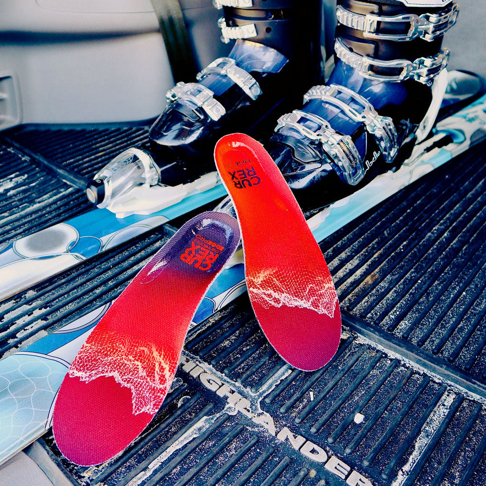 Paire de semelles rouges à profil bas CURREX EDGEPRO à côté des skis et des chaussures de ski #1-choisir-son-profil_low