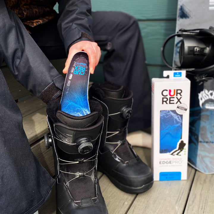 Personne assise sur un banc se préparant à aller skier en plaçant des semelles CURREX EDGEPRO bleues à profil haut dans des bottes de ski noires #1-choix-de-ton-profil_haute