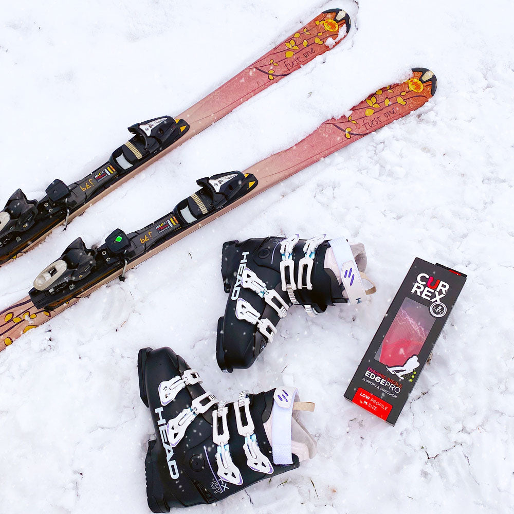 Skis, bottes de ski noires, et chaussettes rouges CURREX EDGEPRO à profil bas assises dans la neige #1-choisir-son-profil_low