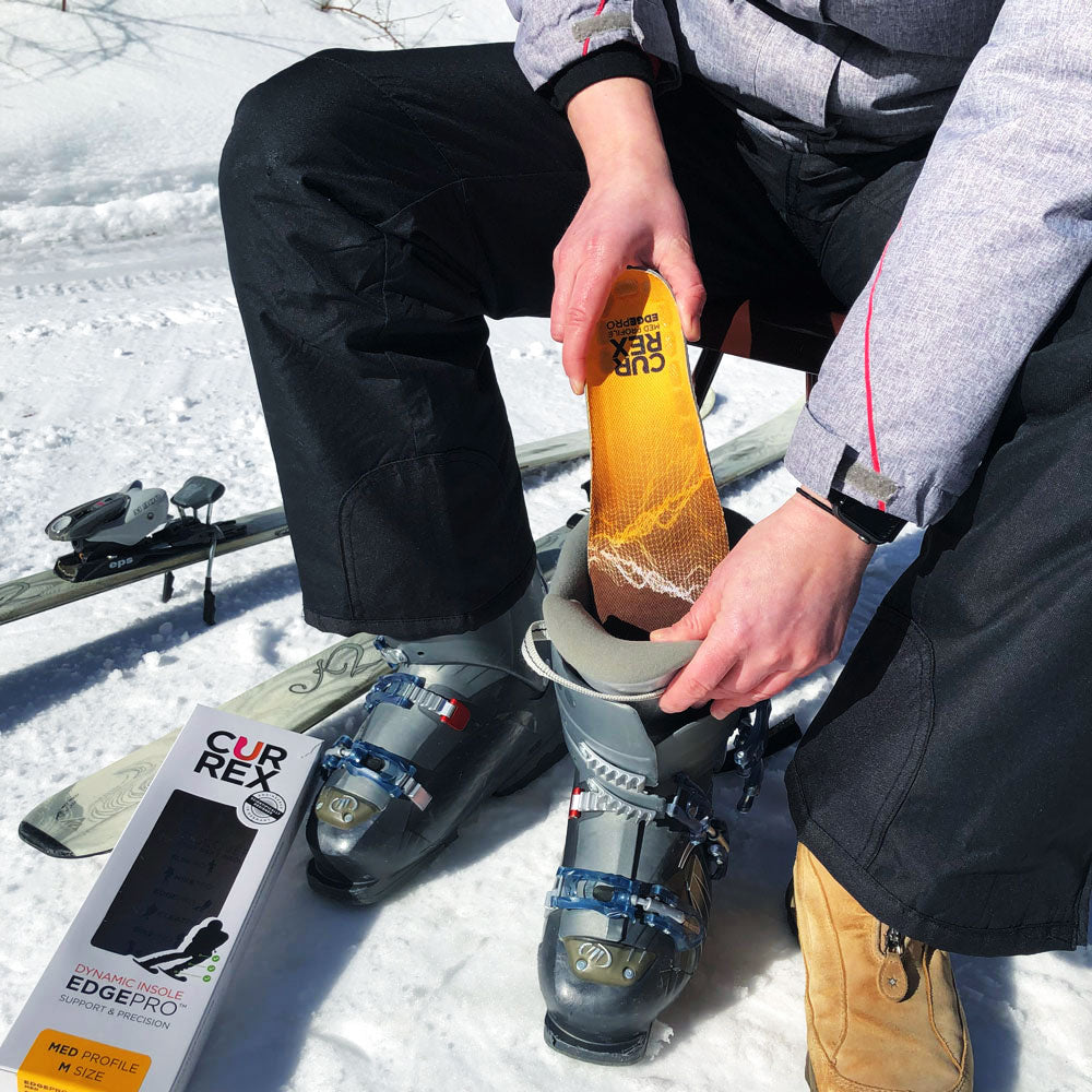 Homme assis sur un siège à côté de skis se préparant à aller skier en ajoutant des semelles CURREX EDGEPRO jaune à profil moyen à ses chaussures de ski #1-wahle-dein-profil_med